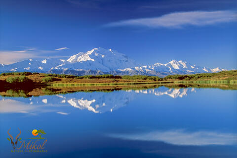 Denail and Alaska range Mountains and clouds reflected in calm lake with  blue sky, white clouds and Fall tundra colors.