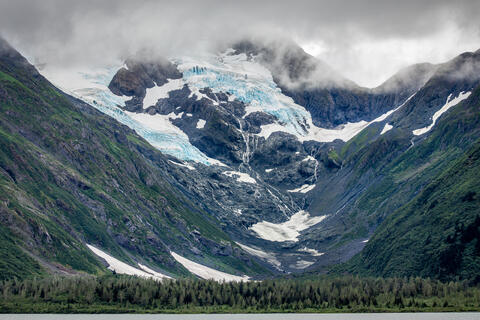 A receding glacier is shown in Alaska, USA, as well as the terminal glacier moraine, a lake, trees, and mountains 