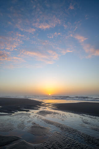 The sun rises at low tide along an Atlantic beach, taken with a wide angler lens 