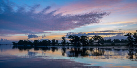 Panoramic view of dawn on a calm day with colorful clouds and trees reflected in the river in south carolina, usa