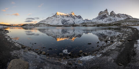 Paine Massif and los cuernos are reflected in a calm, placid lago nordenskjold as seen from mirador cuernos in the winter with snow on the ground. 