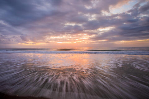 The surf is shown blurred due to a long exposure at sunrise, with pastel colors giving this photograph a soothing effect. 