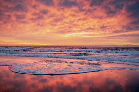 The Sun rises over the Atlantic ocean at dawn lighting up the clouds and the waves which break on the beach.
