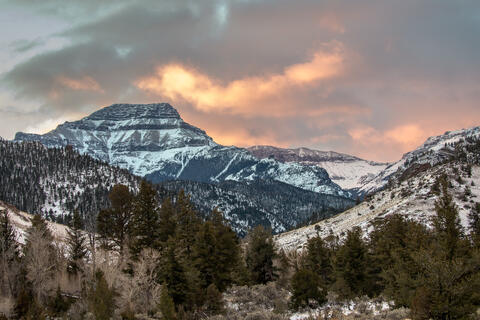 Dawn in the shoshone national forest of Montana lights up the clouds with red and orange colors above the snow covered mountains.