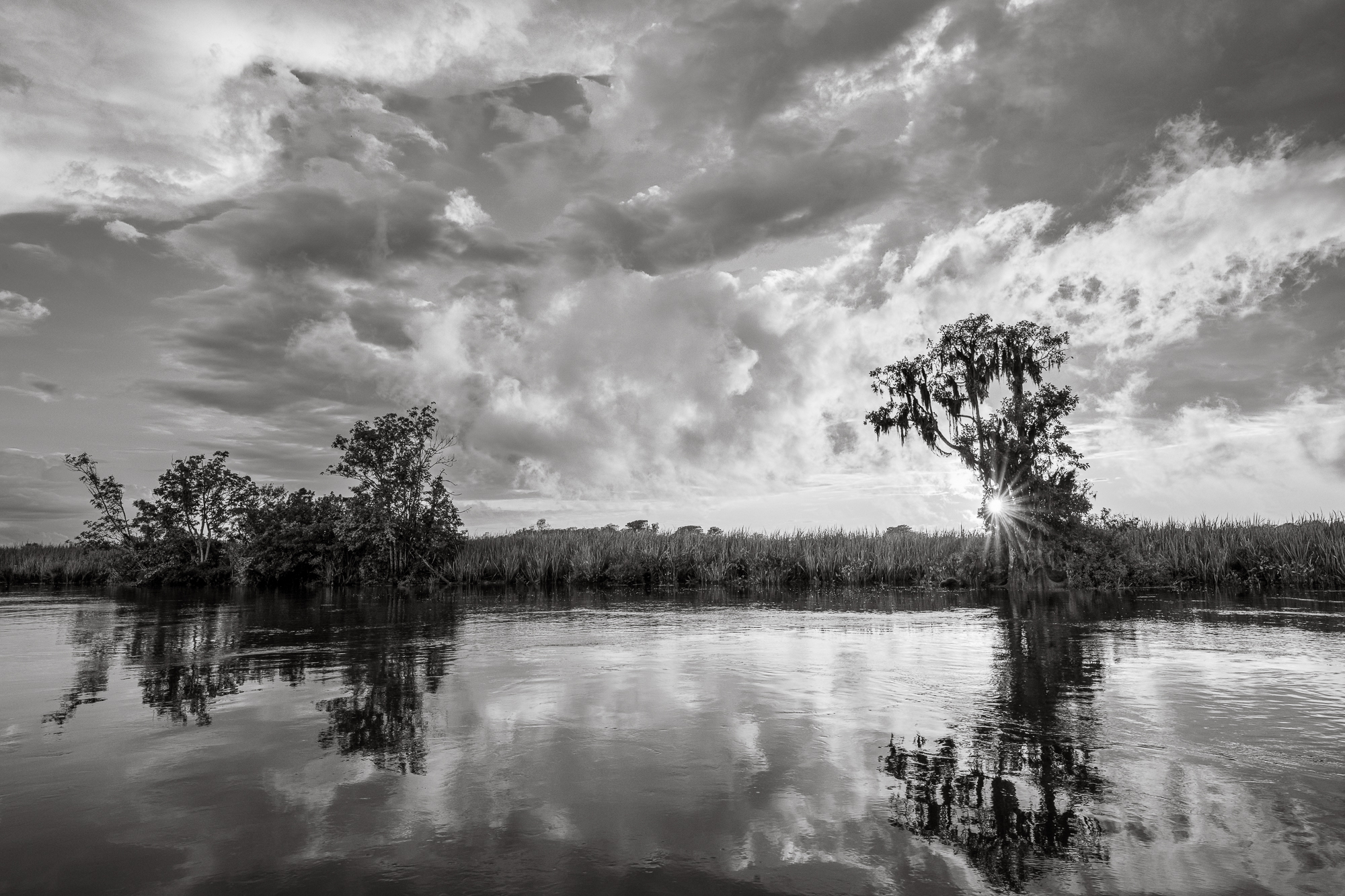 Black Water River Sunset The sun breaks through close to sunset along a black water river after a storm passes, with cypress trees reflected in the placid waters.